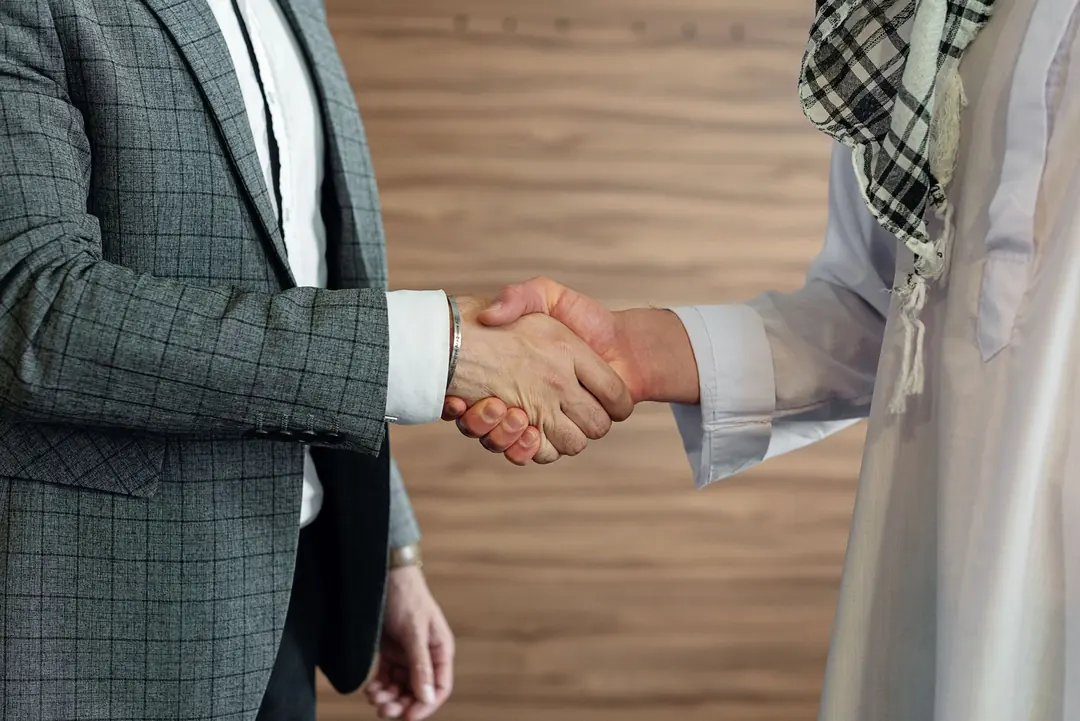 Close-up of a handshake between two men in business attire, one in traditional Middle Eastern dress