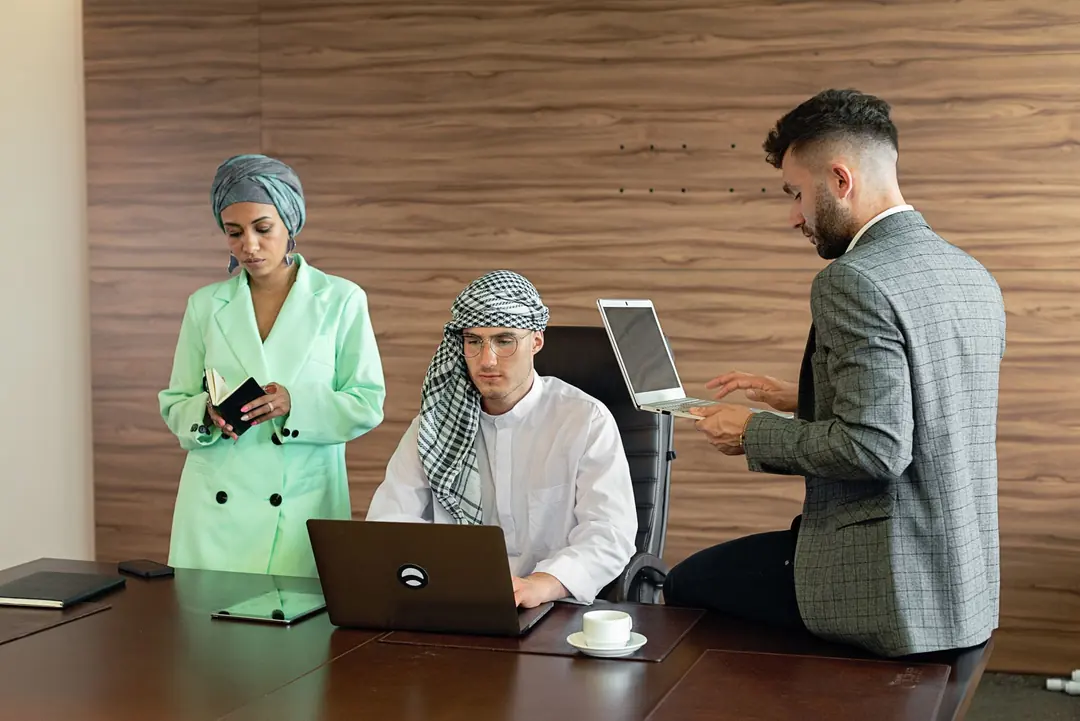 Three colleagues in a meeting room with laptops and a notebook