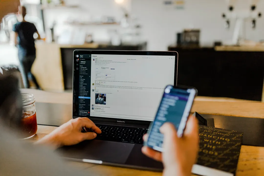 Person checking information on a laptop and a smartphone at a table